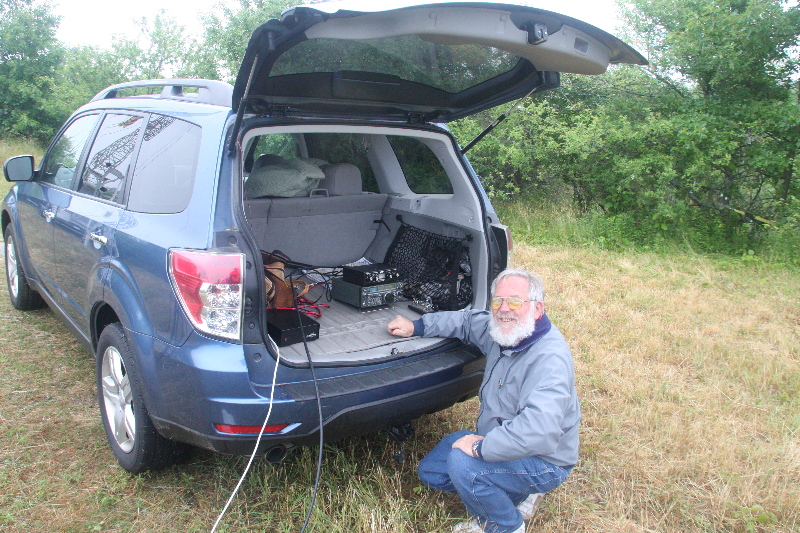 Bob W1XP squatting at the back of his van with an HF radio after participating in the HamSci satellite atmospheric test